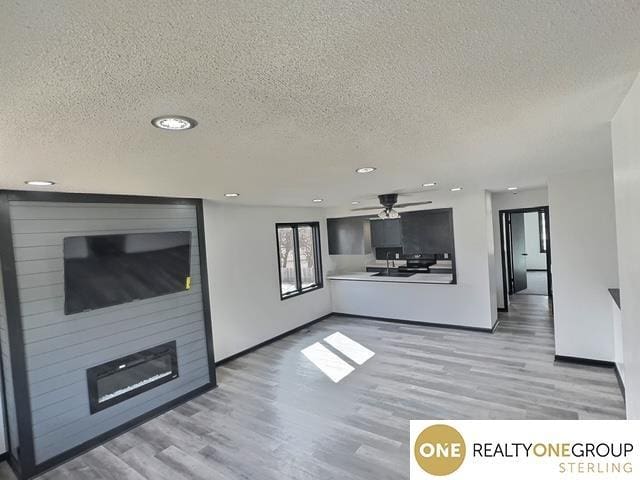 unfurnished living room featuring a large fireplace, baseboards, ceiling fan, wood finished floors, and a textured ceiling