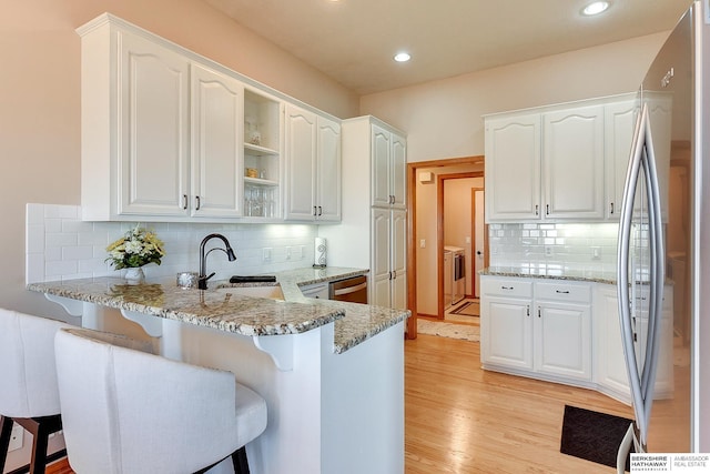 kitchen featuring a sink, a kitchen breakfast bar, washing machine and dryer, a peninsula, and appliances with stainless steel finishes