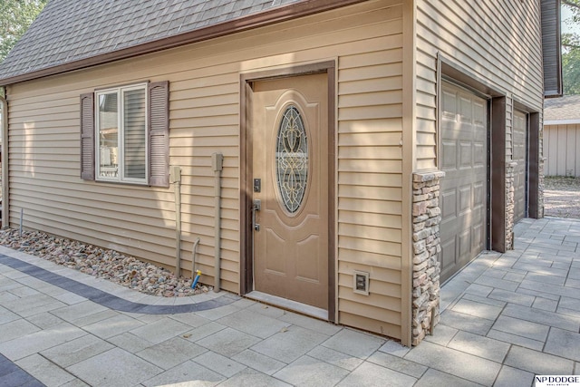 entrance to property featuring stone siding and roof with shingles