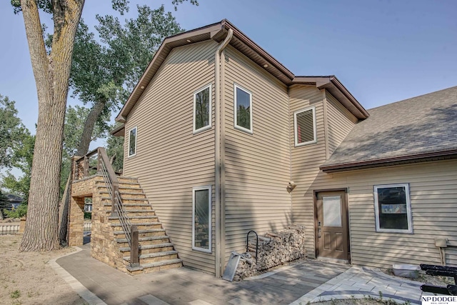 back of house featuring stairway, a patio area, and roof with shingles