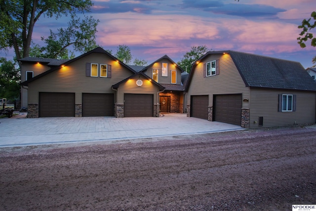 view of front of house with an attached garage, stone siding, driveway, and a gambrel roof