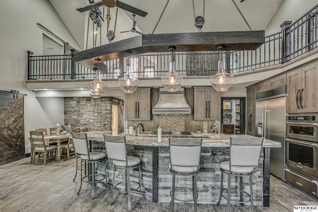 kitchen featuring light wood finished floors, appliances with stainless steel finishes, a kitchen breakfast bar, custom exhaust hood, and a warming drawer