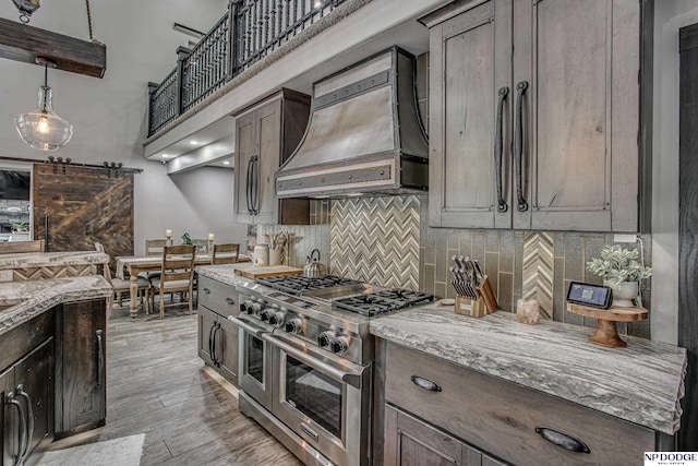 kitchen featuring premium range hood, backsplash, a barn door, light wood finished floors, and range with two ovens