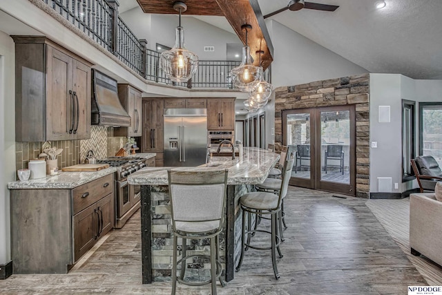 kitchen with a breakfast bar area, light wood-type flooring, french doors, custom exhaust hood, and high end appliances