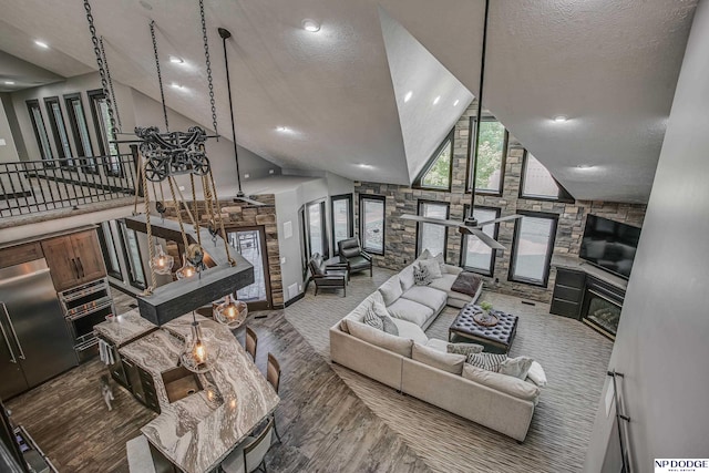 living area featuring a ceiling fan, high vaulted ceiling, stairs, a textured ceiling, and a glass covered fireplace