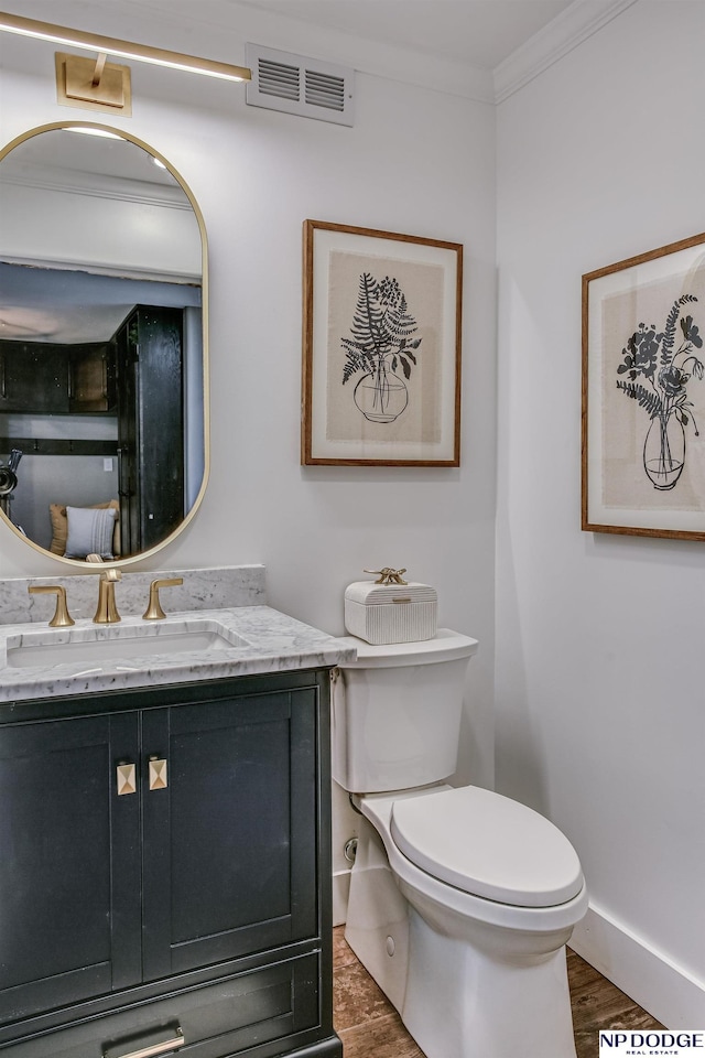 half bathroom featuring vanity, wood finished floors, visible vents, crown molding, and toilet