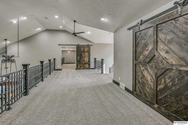 interior space with a barn door, a ceiling fan, visible vents, and lofted ceiling