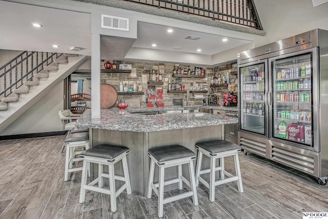 kitchen with a kitchen bar, stone countertops, visible vents, and wood finish floors