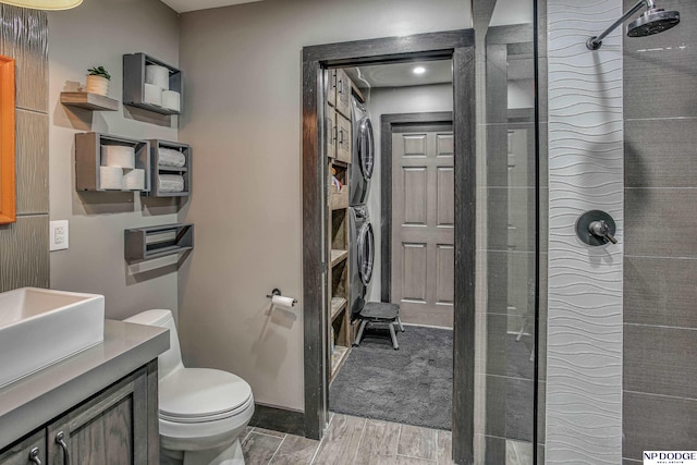 full bathroom featuring wood finish floors, toilet, a tile shower, stacked washer / dryer, and vanity