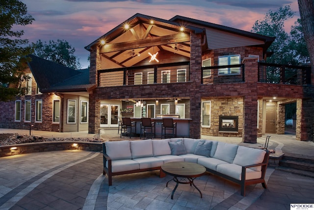 back of property at dusk with an outdoor hangout area, a balcony, a patio, and outdoor dry bar