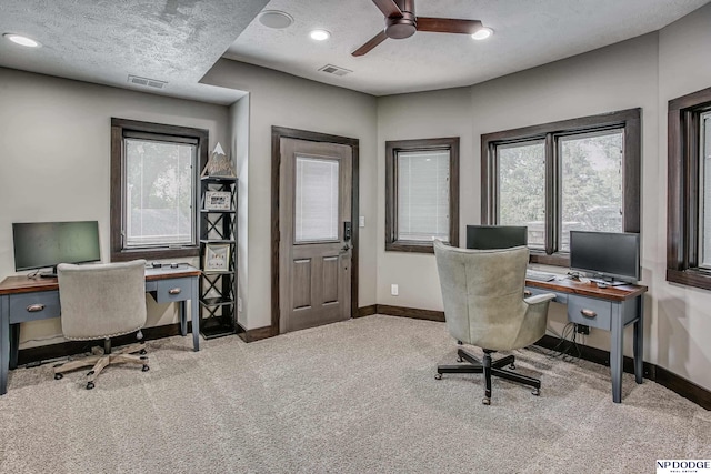 carpeted office space featuring visible vents, baseboards, a textured ceiling, and a ceiling fan