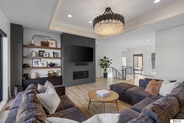 living area featuring light wood-type flooring, a tray ceiling, recessed lighting, an inviting chandelier, and a fireplace