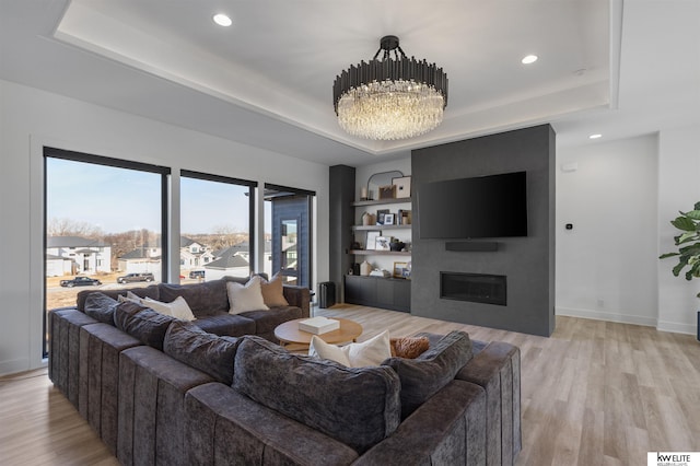 living room with a tray ceiling, a large fireplace, and light wood-style floors