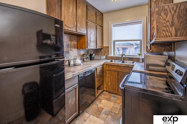 kitchen featuring black appliances, a sink, stone finish flooring, backsplash, and brown cabinetry