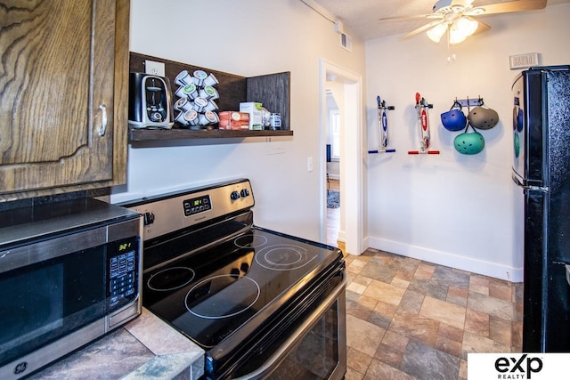 kitchen with baseboards, appliances with stainless steel finishes, ceiling fan, and stone finish floor