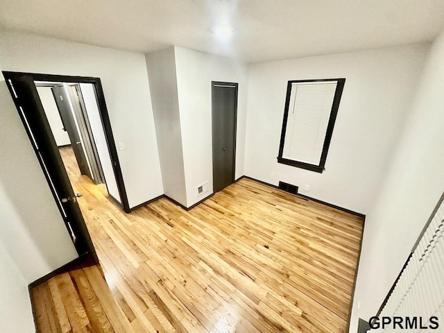 unfurnished bedroom with visible vents, light wood-style flooring, and baseboards