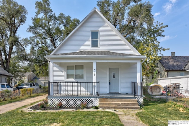 bungalow-style home featuring a porch, fence, a front yard, and a shingled roof