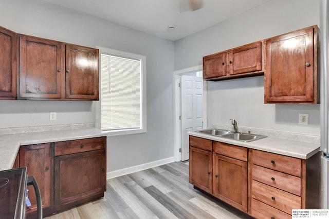 kitchen featuring baseboards, light countertops, light wood-type flooring, electric stove, and a sink