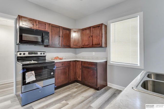 kitchen with a sink, light countertops, stainless steel range with electric stovetop, black microwave, and light wood-type flooring