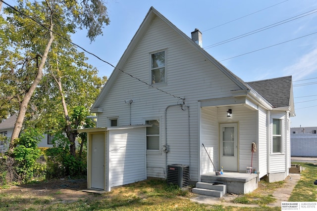 back of house with a chimney, central air condition unit, and a shingled roof