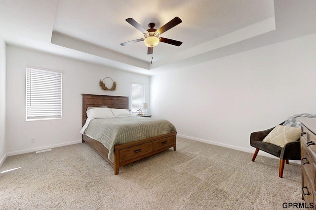 bedroom featuring a tray ceiling, baseboards, light colored carpet, and a ceiling fan