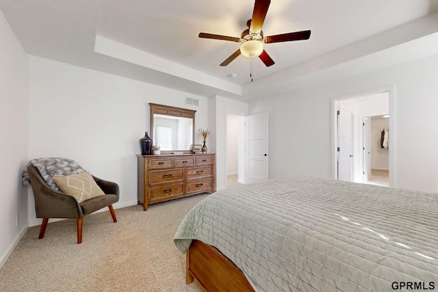 bedroom featuring visible vents, baseboards, light colored carpet, a tray ceiling, and a ceiling fan