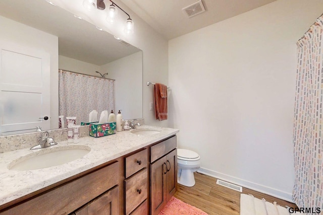 bathroom featuring toilet, wood finished floors, visible vents, and a sink