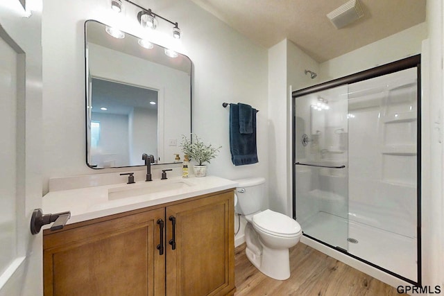 bathroom with visible vents, a shower stall, toilet, wood finished floors, and vanity