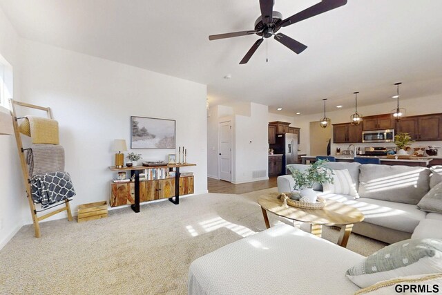 living area featuring baseboards, light colored carpet, visible vents, and ceiling fan