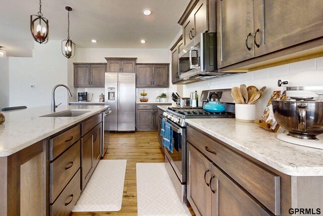 kitchen with light wood-style flooring, recessed lighting, a sink, hanging light fixtures, and appliances with stainless steel finishes