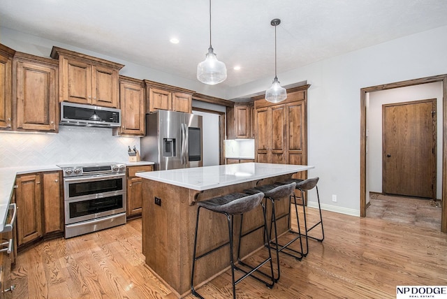 kitchen featuring brown cabinets, light wood-style flooring, a kitchen island, stainless steel appliances, and decorative backsplash