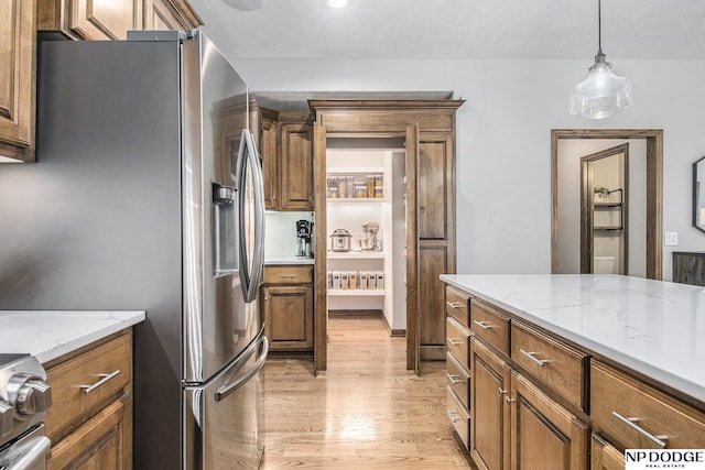 kitchen with brown cabinetry, light wood finished floors, stainless steel fridge with ice dispenser, stove, and decorative light fixtures