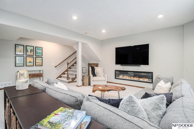 carpeted living room featuring a glass covered fireplace, recessed lighting, stairway, and visible vents