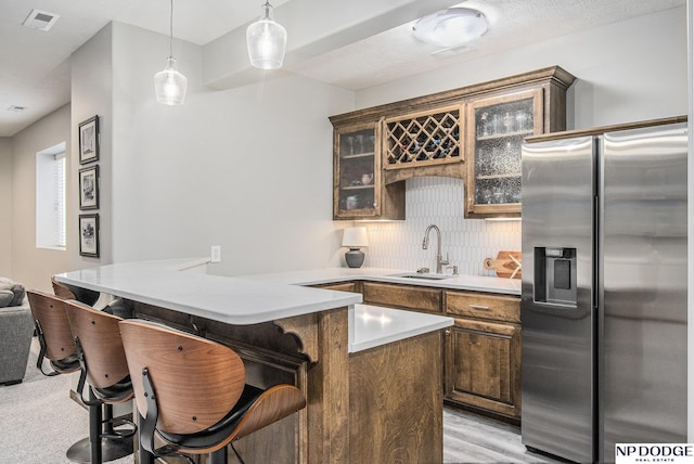 kitchen featuring visible vents, stainless steel refrigerator with ice dispenser, a sink, a kitchen breakfast bar, and glass insert cabinets