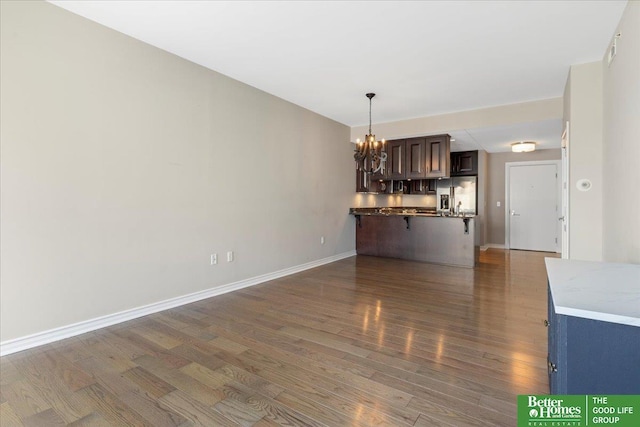 unfurnished living room featuring a notable chandelier, baseboards, and wood finished floors