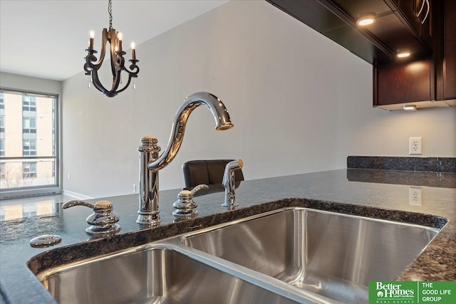 room details with dark brown cabinetry, decorative light fixtures, dark stone countertops, and a sink