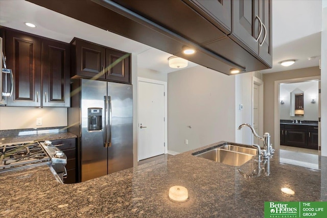 kitchen with a sink, stainless steel appliances, dark brown cabinetry, and dark stone countertops