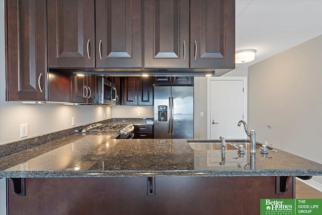 kitchen with a breakfast bar, dark brown cabinetry, appliances with stainless steel finishes, and dark stone counters