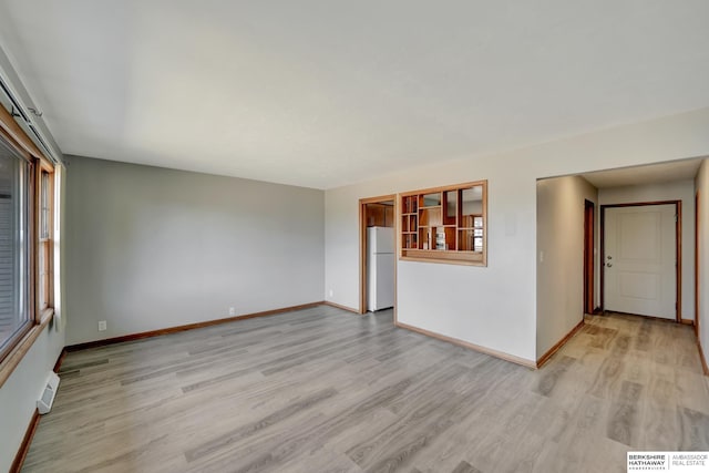 empty room with plenty of natural light, visible vents, baseboards, and light wood finished floors