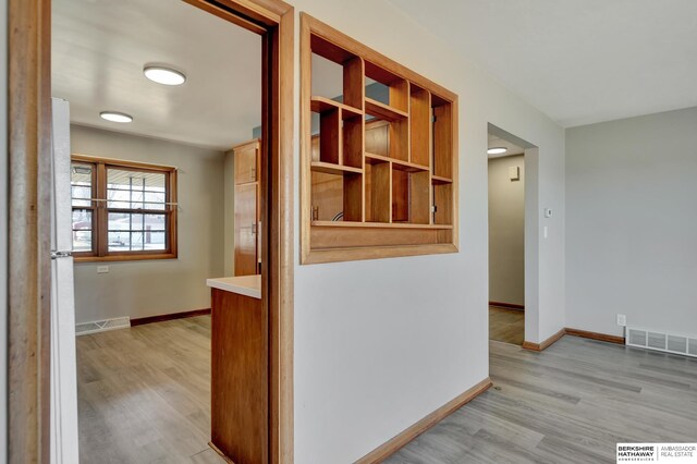 hall with baseboards, visible vents, and light wood finished floors