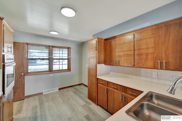 kitchen featuring visible vents, oven, light countertops, decorative backsplash, and a sink