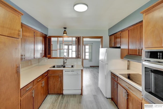 kitchen with under cabinet range hood, light wood-type flooring, decorative backsplash, white appliances, and a sink