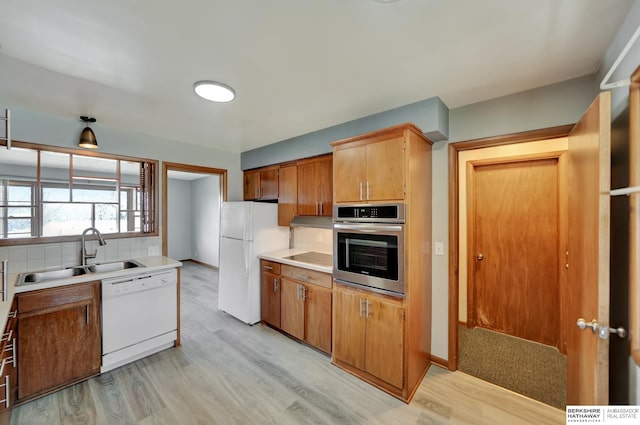 kitchen with light wood-style flooring, a sink, backsplash, white appliances, and light countertops