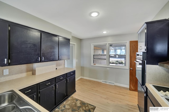 kitchen with light wood finished floors, visible vents, oven, light countertops, and dark cabinetry