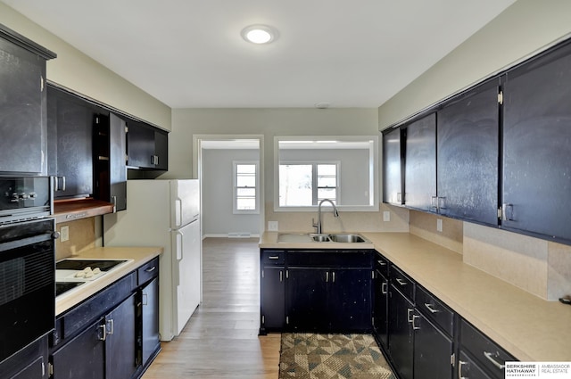 kitchen with light countertops, light wood-style flooring, white appliances, and a sink