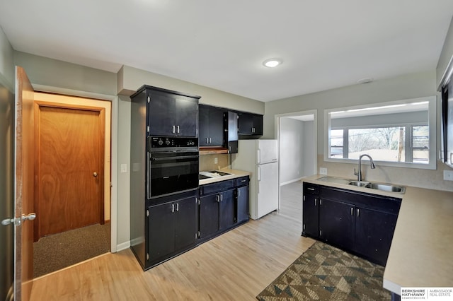 kitchen featuring oven, dark cabinetry, a sink, and freestanding refrigerator