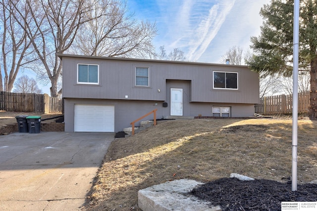 raised ranch with concrete driveway, an attached garage, and fence