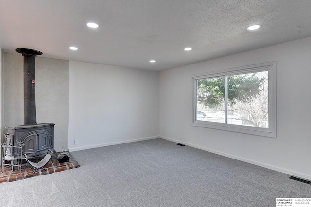 living area featuring carpet, visible vents, baseboards, a wood stove, and recessed lighting