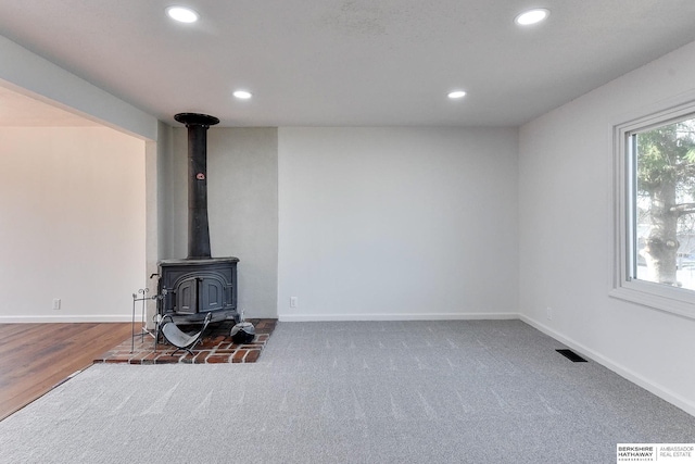 carpeted living area featuring visible vents, a wood stove, recessed lighting, and baseboards