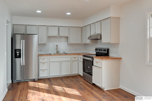 kitchen with a sink, under cabinet range hood, stainless steel appliances, wood-type flooring, and decorative backsplash